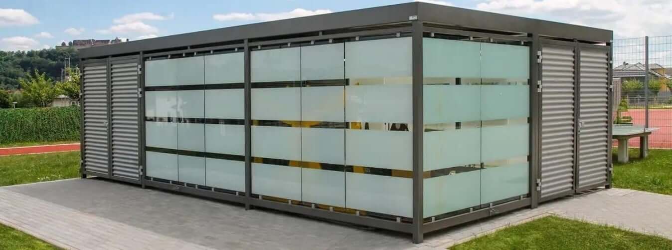 Gesloten fietsenberging met glazen wanden en metalen lamellen geplaatst op een bedrijventerrein.
