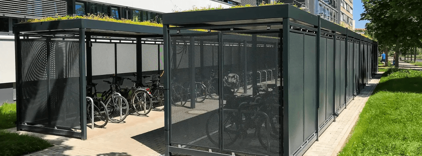 Fietsoverkapping met sedumdak en gesloten wanden voor veilige fietsenstalling geplaatst bij een kantoorgebouw.