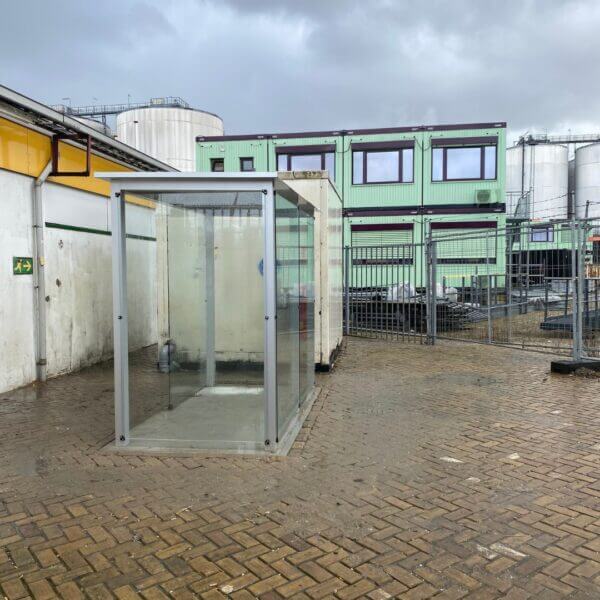 Rokersruimte-buiten-270x150-direct-aanschaffen Compacte rookabri met beschutting tegen regen en wind, geplaatst op nieuwe bestrating op een industriële omgeving.