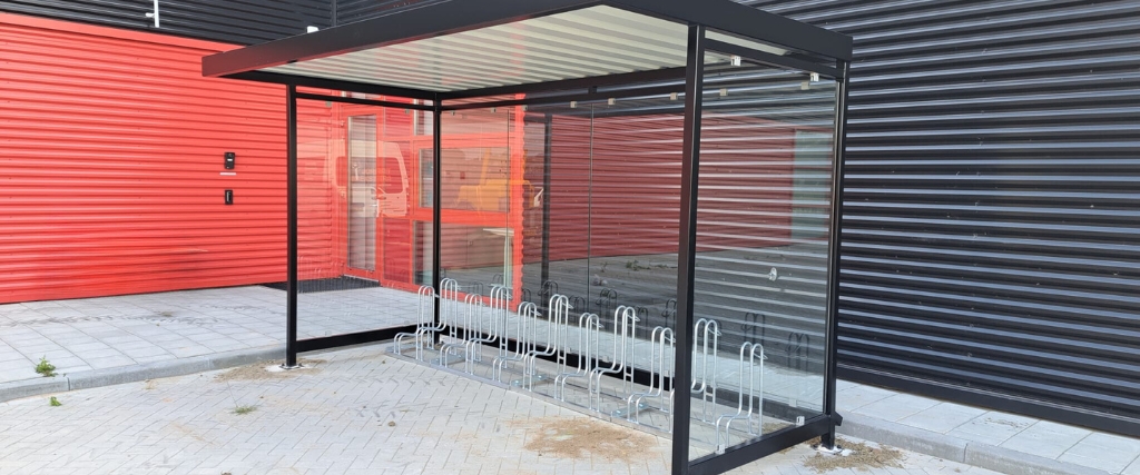Moderne fietsoverkapping van Umfeldt met geïntegreerde fietsenrekken, geplaatst bij een bedrijfsgebouw in Nederland.