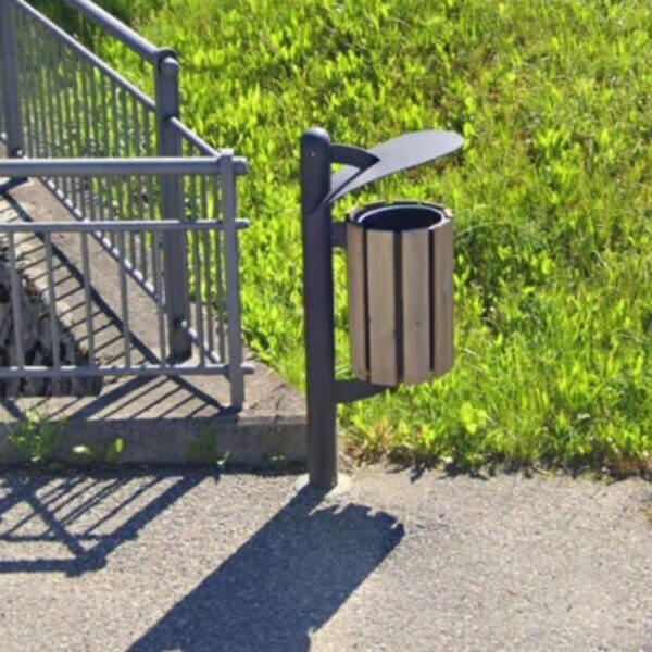 Afvalbak voor buiten kopen met dakje en 45 liter Afvalbak voor buiten met houten bekleding en dakje, gemonteerd aan een paal naast een metalen hekwerk.