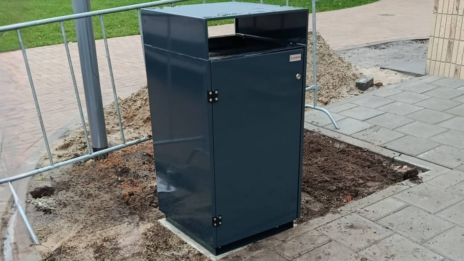 Afvalbak voor buiten 180 liter gepoedercoat in RAL 7016 antracietgrijs, geplaatst op bestrating in openbare ruimte.