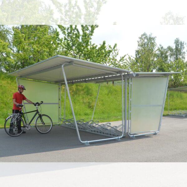 bouwpakket fietsenstalling met fietsenrekken bestellen Budget overdekte fietsenstalling met optionele zijwanden en verzinkte hoog-laag fietsenrekken, gebruikt door een fietser met helm.