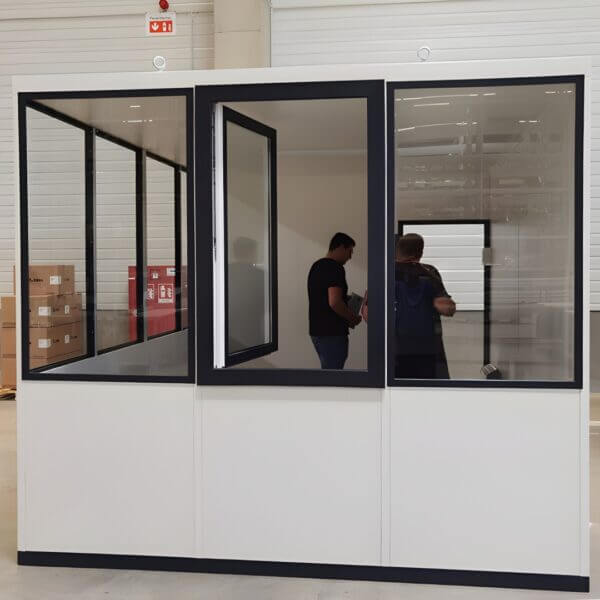 Modulaire Kantoorunit Direct Kopen Modulaire kantoorunit voorzien van veel ramen en geplaatst in een hal, in de kantoorunit staan 2 personen