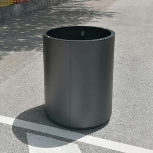 ronde-plantenbak-voor-buiten-cilinder Ronde stalen plantenbak in antracietkleur, geplaatst op een verharde ondergrond in de openbare ruimte