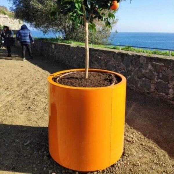 Grote ronde plantenbak kopen voor de openbare ruimte Ronde oranje stalen plantenbak met boom, geplaatst in openbare ruimte met uitzicht op zee