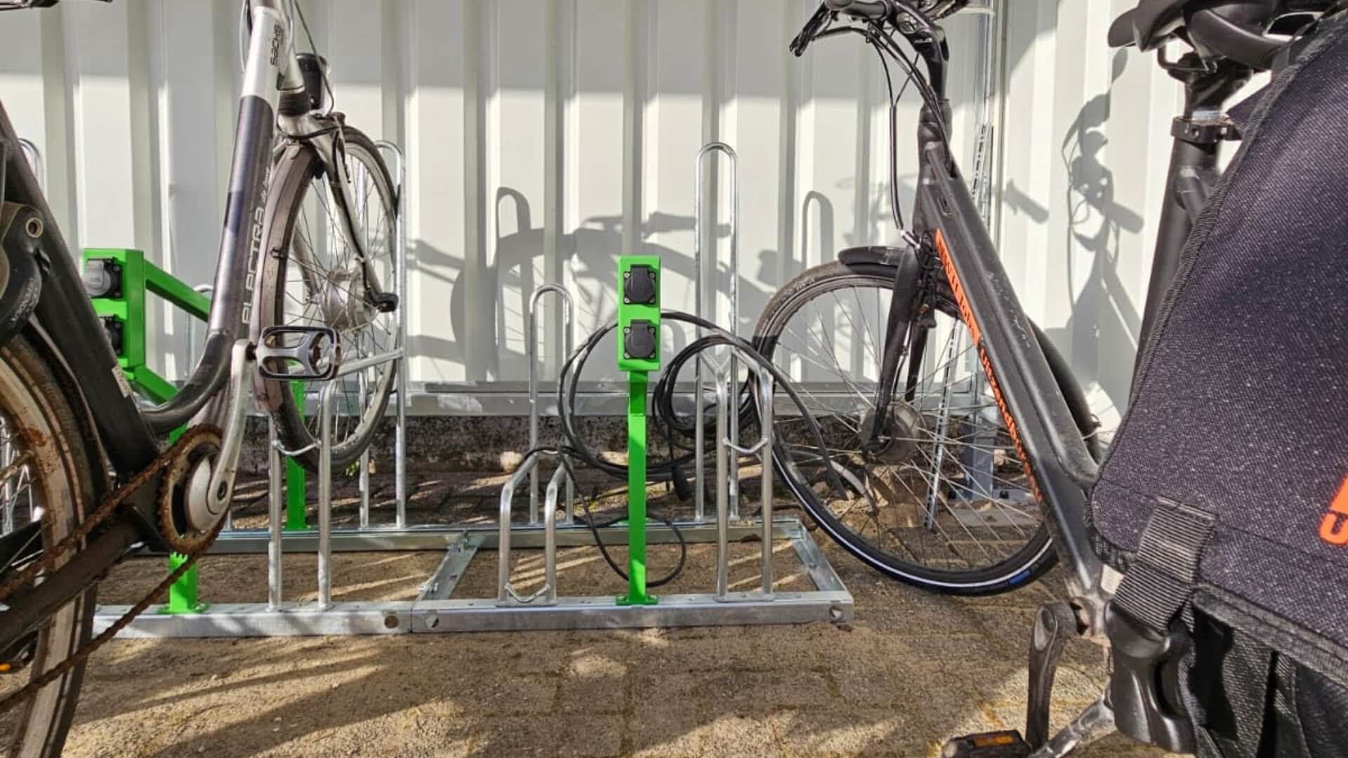 Fietsenrek met geïntegreerde e-bike oplaadpunten, voorzien van verzinkte wielbeugels en groene laadunit, gebruikt voor het veilig parkeren en opladen van fietsen.