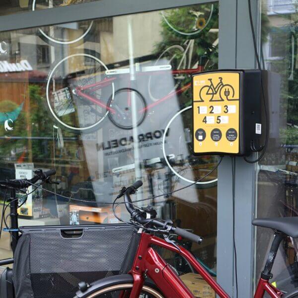 Laadstation voor Fietsenstalling – Efficiënt Oplaadpunt voor E-bikes Laadstation voor elektrische fietsen, wandgemonteerd bij een fietsenstalling, met meerdere oplaadpunten.