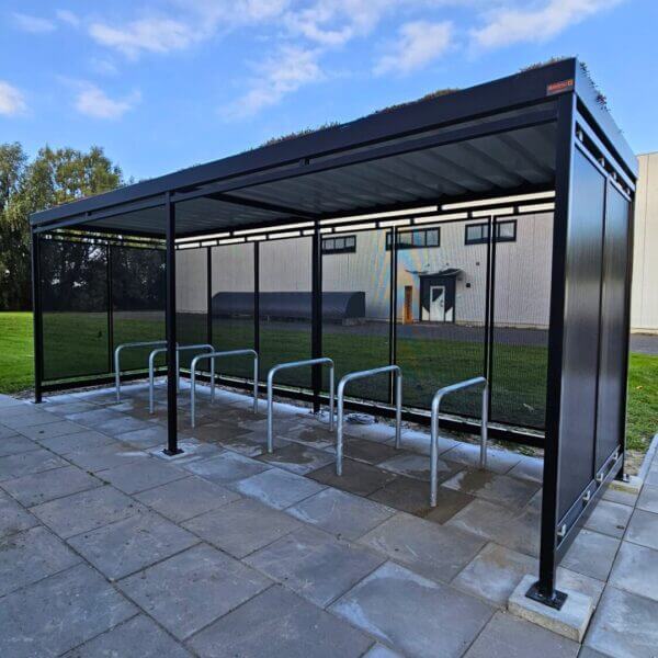 rijwieloverkapping-kopen-geperforeerd-staal Rijwieloverkapping van Umfeldt met geperforeerde stalen wanden, fietsaanleunbeugels en een sedumdak geplaatst op terrein van Online Veiling Meester.