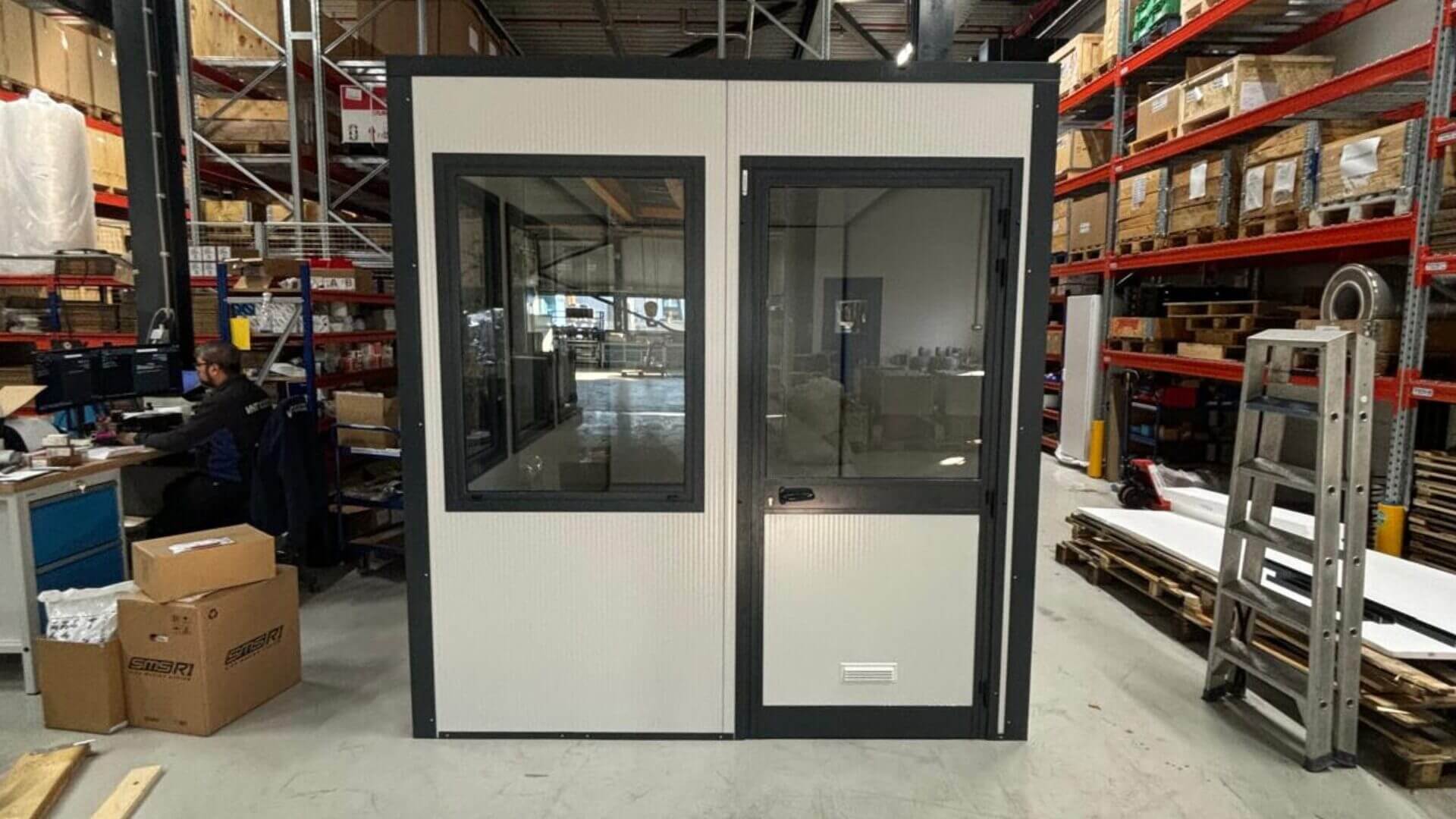 Prefab bureelunit met raam en deur in magazijn geplaatst in een opslagruimte.