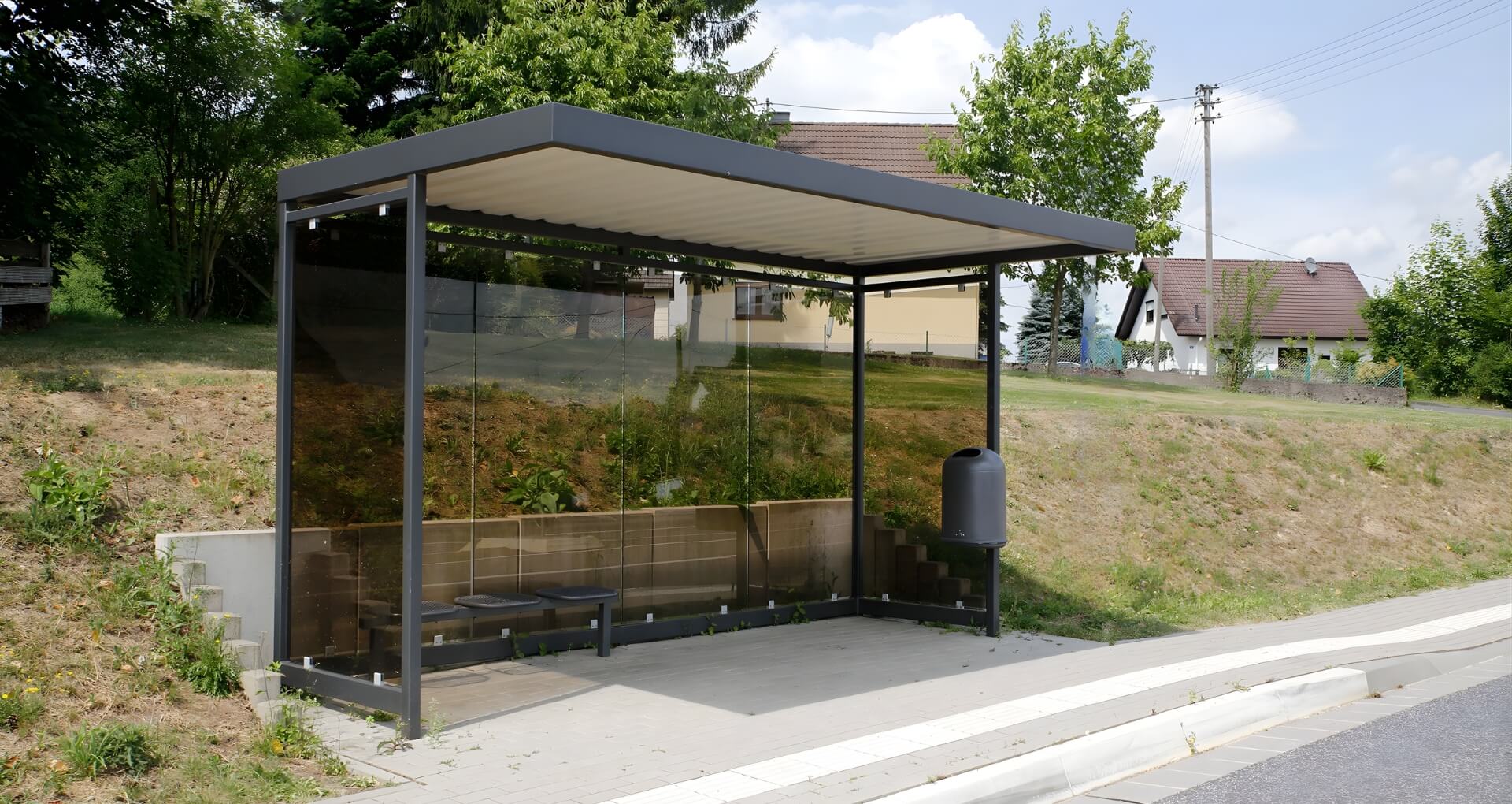 Transparante rokersoverkapping met donker frame langs een weg in een groene woonomgeving